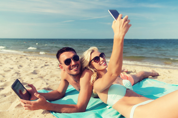 happy couple with modern gadgets lying on beach - Fotoğraf, Görsel