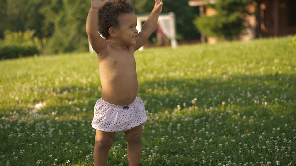 Happy Afro-American little girl learning to walk on the green grass - Footage, Video