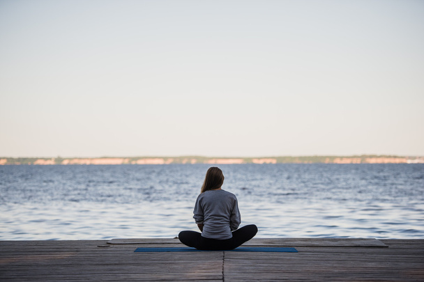 Женщина медитирует в Lotus Pose на пирсе с видом на море. Падмасана. Концепция отдыха
 - Фото, изображение