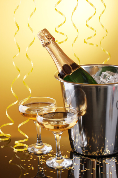 Champagne bottle in bucket with ice and glasses of champagne, on yellow background - Φωτογραφία, εικόνα