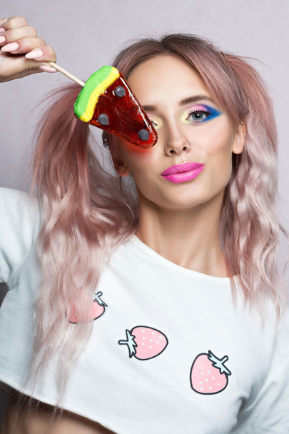 Piękno modelu z dwóch różowy kucyk fryzura jedzenia kolorowy lizak. - Zdjęcie, obraz