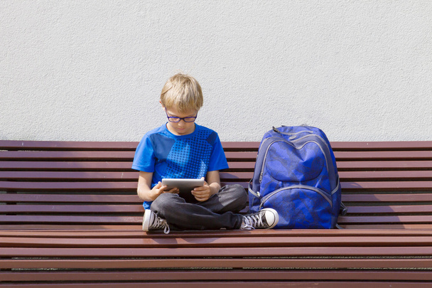 Boy with glasses using tablet PC. Child sitting on the bench. Outdoor. Free copy space. Education, technology, people concept - Photo, image