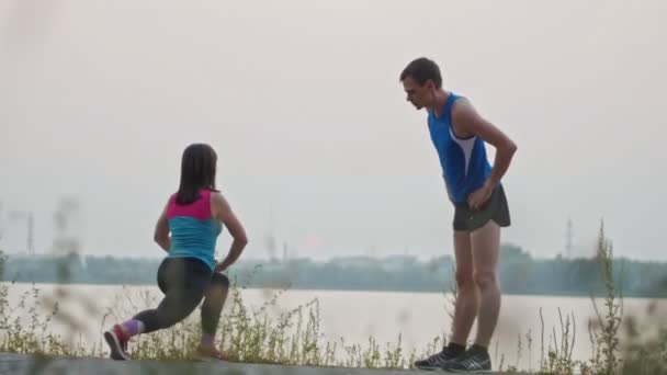 Couple stretching together in the park at dusk, over the river - Materiał filmowy, wideo