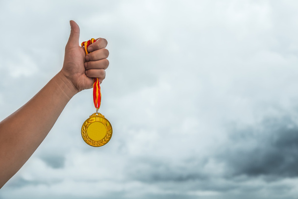 мужчина поднимает золотую медаль большим пальцем вверх - Фото, изображение