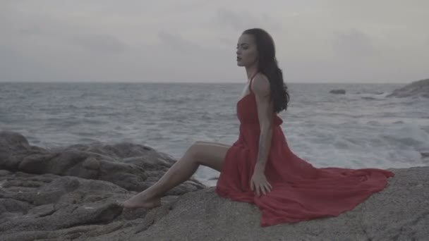 Красивая соблазнительная женщина в красном платье наслаждается жизнью на скалах у моря  - Кадры, видео