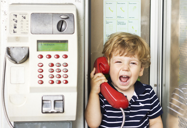 Ένα μικρό αγόρι που φωνάζει στο τηλέφωνο. Παιδί ουρλιάζοντας στο κόκκινο ακουστικό τηλέφωνο - Φωτογραφία, εικόνα