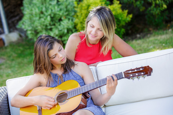 Ładna dziewczyna gra na gitarze w ogrodzie z jej mama - Zdjęcie, obraz