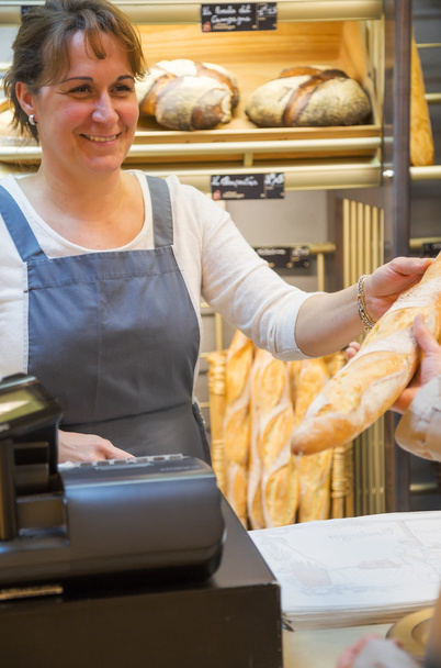 улыбающаяся женщина в фартуке продает хлеб в пекарне
 - Фото, изображение