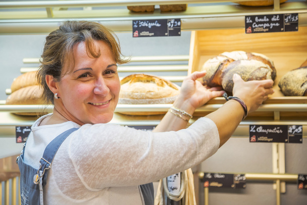 mujer sonriente con un delantal vendiendo pan en una panadería
 - Foto, Imagen