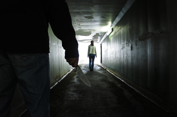Die Silhouette eines Mannes trägt ein Messer und folgt einer jungen Frau in einem dunklen Tunnel. Gewalt gegen Frauen. echte Menschen, Kopierraum - Foto, Bild