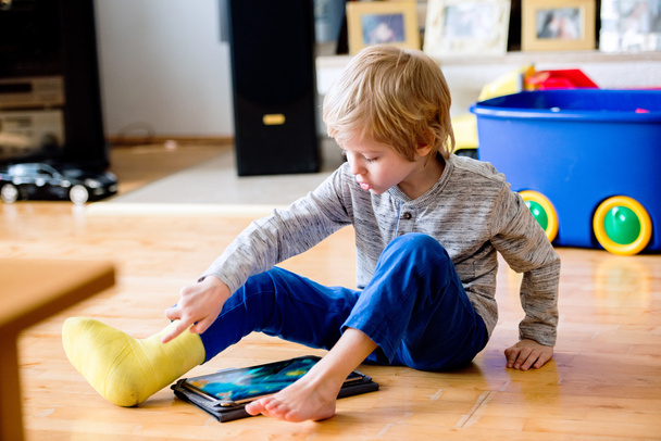Boy with broken leg  playing on tablet. - Fotó, kép
