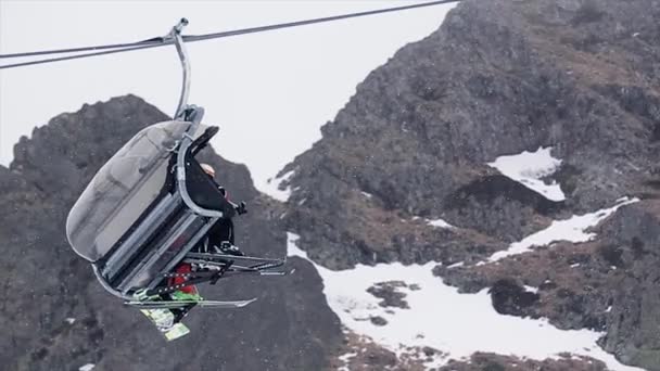 Ski lift emberekkel felcsúszik a havas hegyek. Sí resort. Hó esik. Snowboard. Nyitott kabin - Felvétel, videó