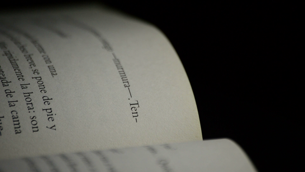 Textos e palavras de página de papel de livro aberto em espanhol girando em fundo preto
 - Filmagem, Vídeo
