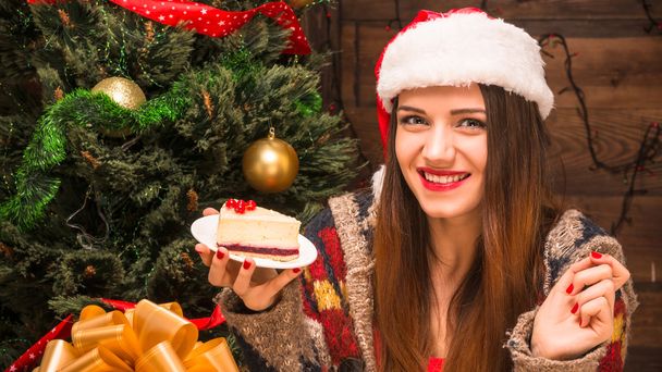 Beautiful girl sitting near New Year tree and eating delicious cake - Foto, immagini