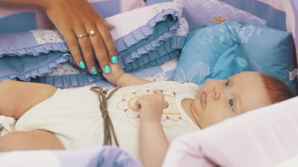 Mother hold hand little baby lie in crib watching colorful moving toys above him - Video