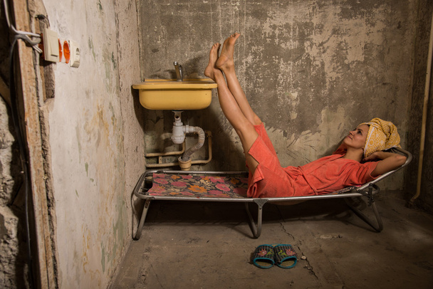 Cheap accommodation. The girl lies in a bed in an old apartment - Foto, afbeelding