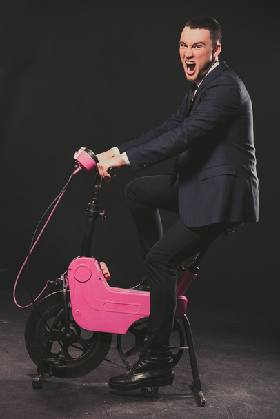 Model. A man in a business suit pedaling on a stationary bike. - Zdjęcie, obraz