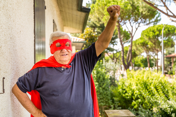 senior haciéndose pasar por superhéroe con capa roja y máscara
 - Foto, imagen