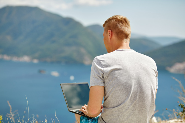 Молодий фрілансер, який використовує ноутбук, сидить біля моря. Щасливий усміхнений чоловік, що працює онлайн. Вивчення та навчання за допомогою ноутбука. Фрілансова робота, концепція бізнесменів
. - Фото, зображення