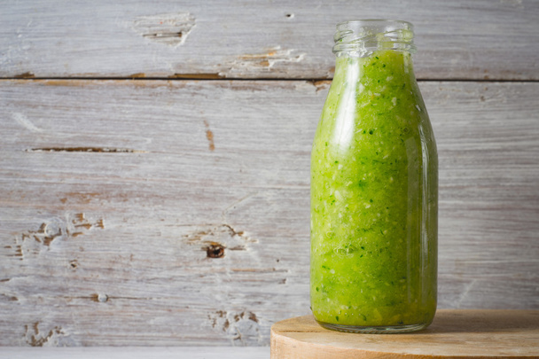 Green smoothie in the glass bottle on the white wooden background - Фото, изображение