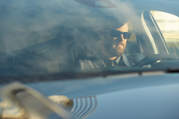 Handsome serious man in black glasses drives a car - Foto, Imagen