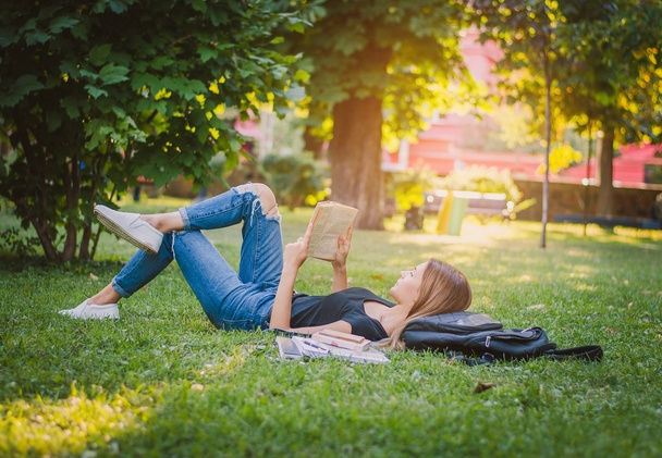 chica estudiante en un parque acostado en la hierba y la lectura de un libro, ly
 - Foto, Imagen