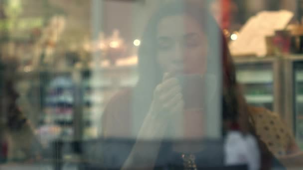 Gyönyörű barna lány forró csokoládé ivás kis kávézóban. Nézd, az ablakon kívül. 4k videóinak - Felvétel, videó