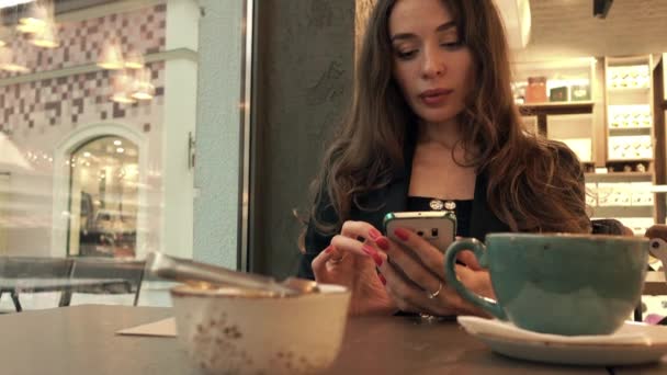 Hermosa mujer joven usando su teléfono inteligente en la cafetería. Vídeo 4K
 - Imágenes, Vídeo