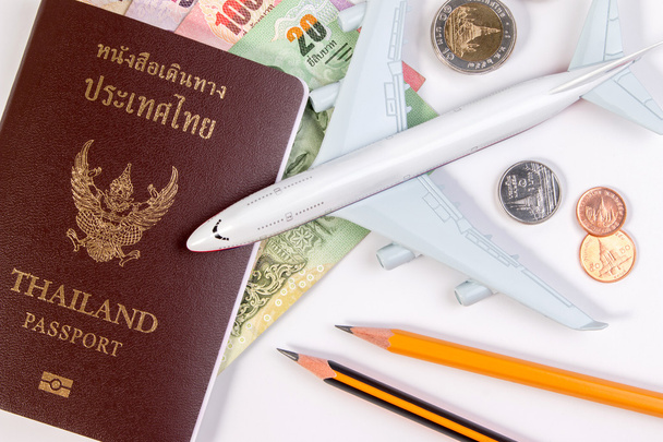 Pasaporte tailandés con billete de dinero tailandés, moneda tailandesa y avión. El pasaporte del ciudadano tailandés y el billete tailandés sobre fondo blanco
. - Foto, imagen