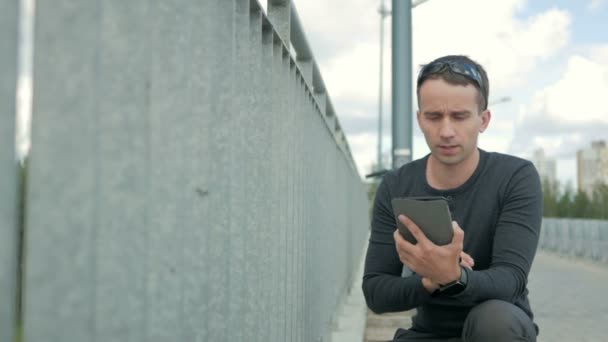 Ulkona muotokuva modernin nuoren miehen digitaalinen tabletti. Sillan kaide, tien lähellä ja kauniit siniset pilvet taustalla
 - Materiaali, video