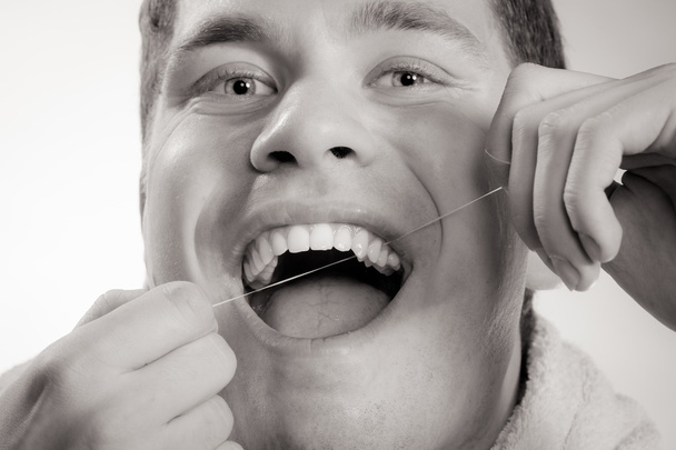 Молодий чоловік чистить білі зуби зубною ниткою
 - Фото, зображення