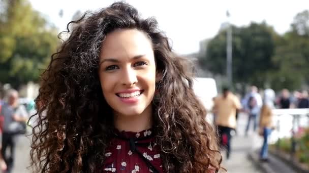 Портрет красивой молодой женщины с вьющимися волосами, улыбающейся в городе, замедленная съемка
 - Кадры, видео
