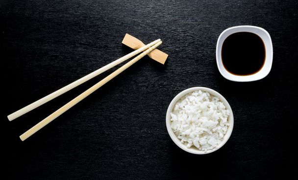 Palillos de sushi japoneses sobre un tazón de salsa de soja, arroz en bac negro
 - Foto, imagen