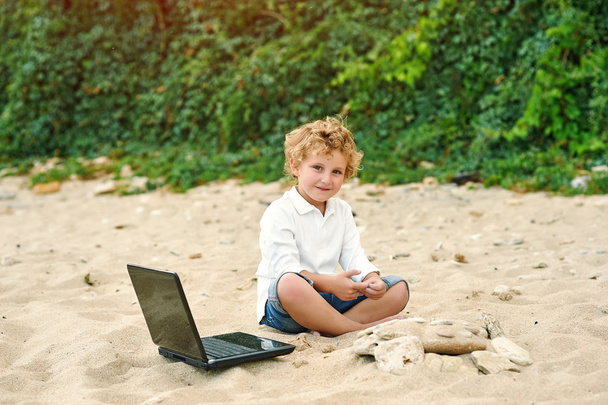 egy kisfiú játszik a tengerparton, a laptop mellett fekve - Fotó, kép