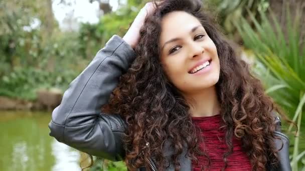 Onnellisen nuoren naisen muotokuva, jolla on kauniit kiharat hiukset hymyillen puistossa, hidastettuna
 - Materiaali, video