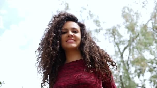Πορτραίτο μιας ευτυχης νεαρής γυναίκας με όμορφα σγουρά μαλλιά που χαμογελούν σε ένα πάρκο, αργή κίνηση - Πλάνα, βίντεο