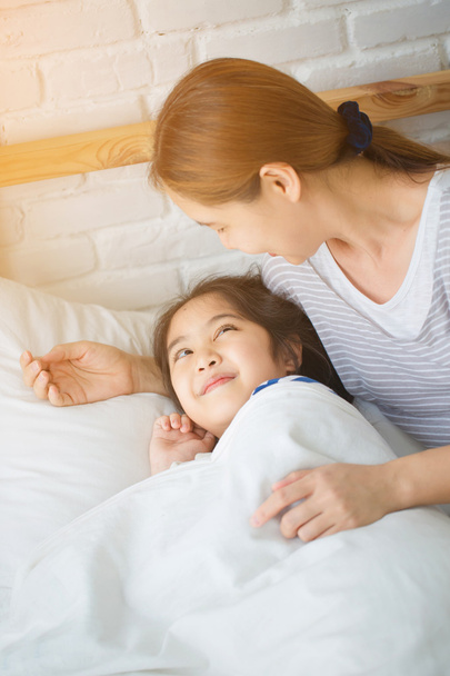 Aziatische moeder haar dochter op het bed in de ochtend wakker - Foto, afbeelding