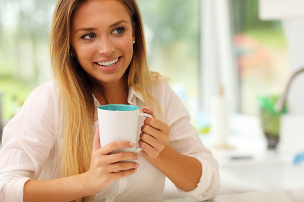 Young woman with coffee in kitchen - Foto, Imagen
