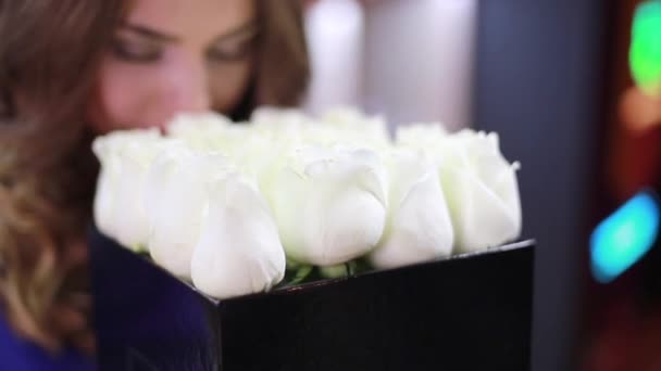 Молодая красивая девушка нюхает цветы и сотрит в камеру
. - Кадры, видео