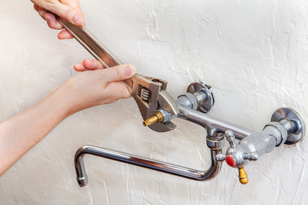 Hands of a plumber fixing a tap in the kitchen - Фото, изображение