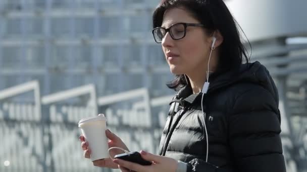 Girl With Coffee Talk on the Phone. Girl in a Black Jacket and Glasses - Filmati, video