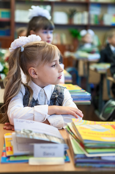 Schoolgirl with folded hand sitting at school desk and listening - Фото, зображення
