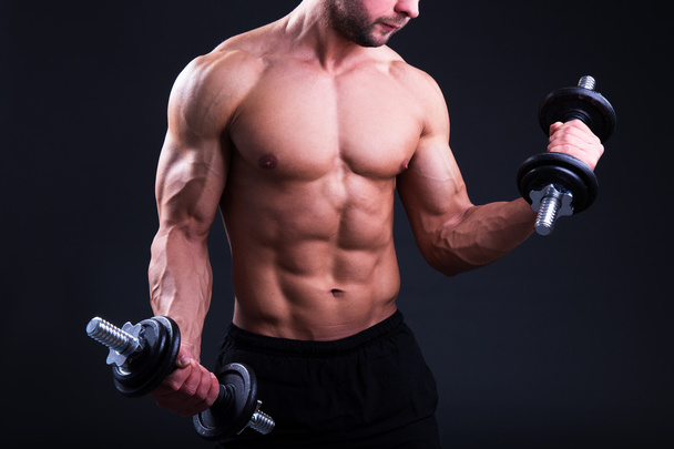м'язове тіло молодого чоловіка позує з гантелями над сірим
  - Фото, зображення