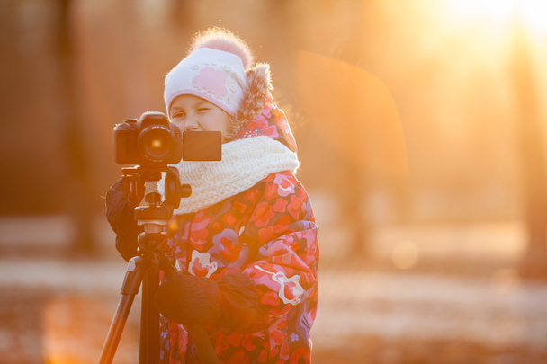 Young child photographer taking pictures on camera using a tripod, sunset light, copyspace - Fotografie, Obrázek