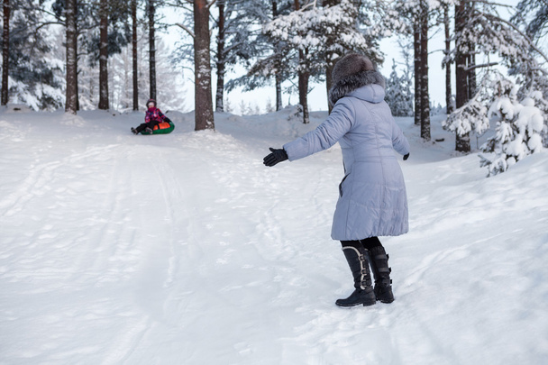 Woman catching child tubing on downhill in winter forest - 写真・画像