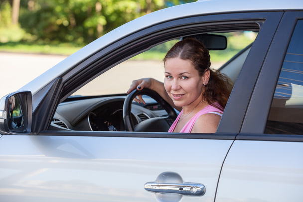 Pretty Caucasian woman sitting in suv, holding wheel and looking at camera - Photo, image
