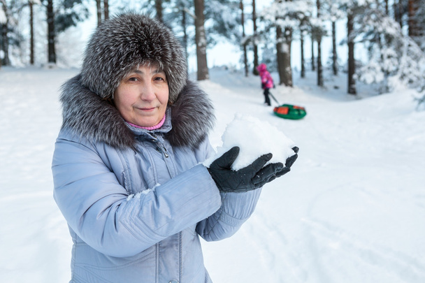 Mature Caucasian woman holding snow in hands while standing in tube downhill in forest - Fotó, kép