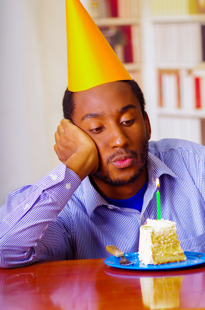 Hombre reflexivo con camisa azul y sombrero sentado junto a la mesa con un pedazo de pastel en frente, mirando triste, celebrando solo el concepto
 - Foto, imagen