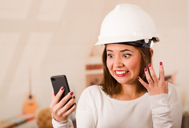 Young woman wearing construction helmet looking at mobile phone with stressed facial expression - Foto, Imagem