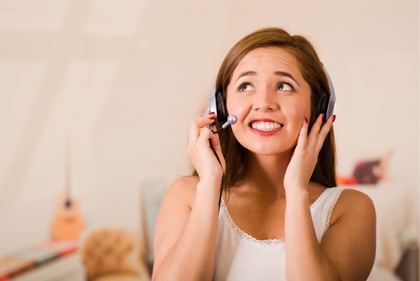 Young woman wearing white top and headset facing camera while interacting smiling, stressed concept - Foto, imagen